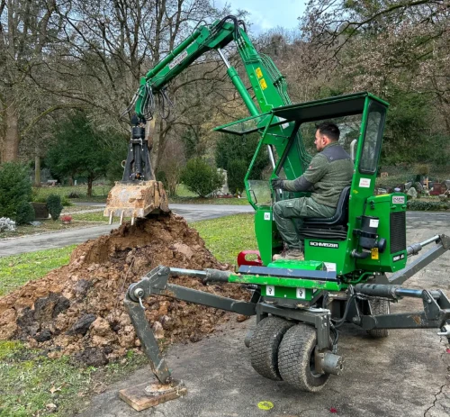 Mann in einem grünen Bagger hebt ein Grab aus